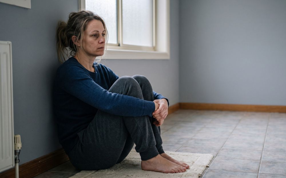 Woman sitting alone at home, reflecting on years of unspoken pain after a third degree tear during childbirth